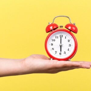 Piros retro ébresztőóra kézben sárga háttér előtt.